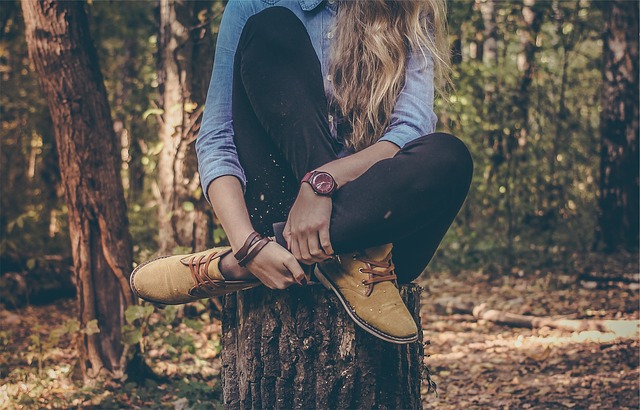 Une femme aux cheveux longs est assise sur un tronc d'arbre, dans la forêt.