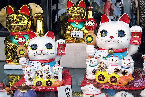 Des figurines maneki-neko, porte-bonheurs japonais symbolisés par un chat qui lève une patte, dans une vitrine.