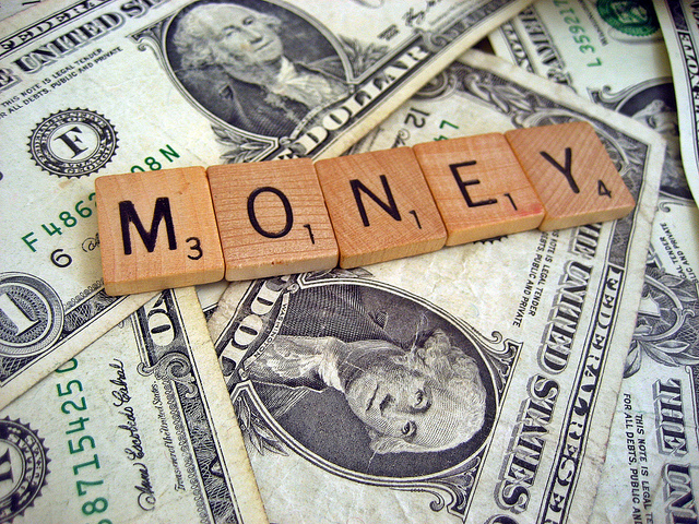 Photographie du mot "MONEY" composé avec des lettres de scrabble sur un tas de billets de banque.