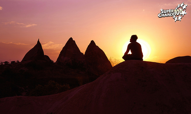 Photographie d'un paysage montagnard pendant le coucher du soleil avec un homme en train de méditer.