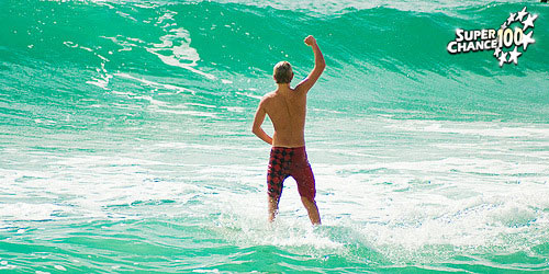 Photographie d'un homme en maillot de bain le poing levé face à une mer paradisiaque.