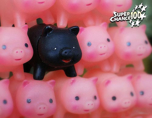 Photographie de figurines de cochon rose superposés avec un cochon noir dans le tas.