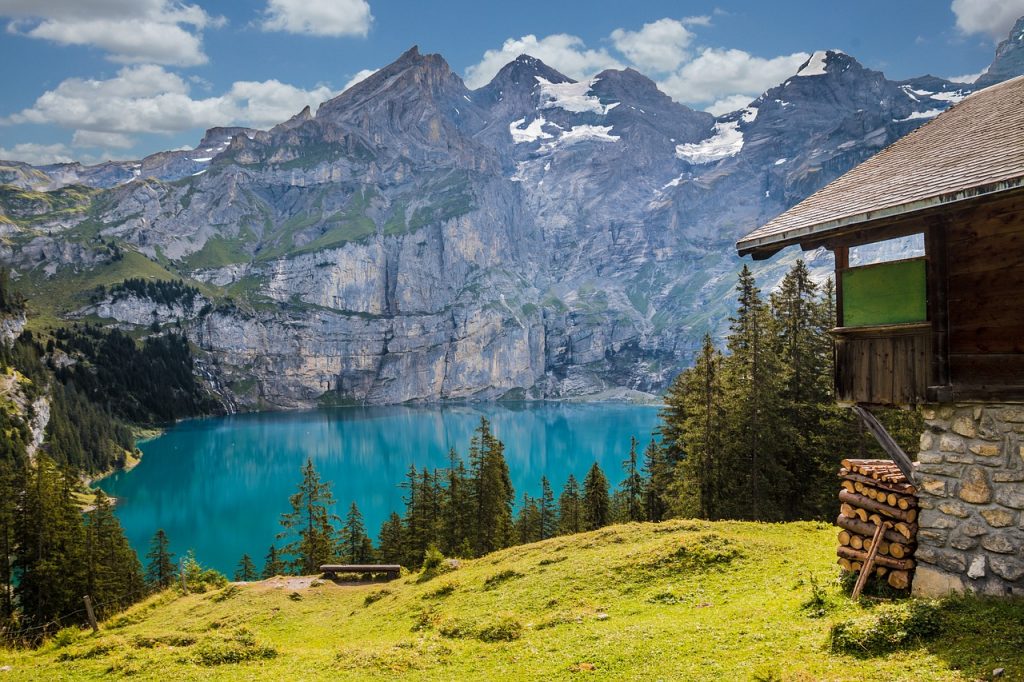C'est un paysage suisse avec un lac et une petite maison sur la droite , et des montagnes au loin.